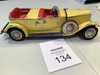 Side view of vintage yellow metal toy truck with red interior seats and wire-spoke wheels, showing paint chipping and wear.