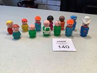 Twelve Fisher-Price vintage Little People figurines arranged on a tabletop showing variety of characters and colors.