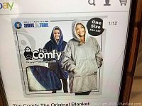 Promotional image showing male and female models wearing The Comfy original blanket sweatshirt hoodie in blue and gray colors, highlighting oversized fit, hood, and front pocket.