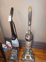 Photo showing Dirt Devil Easy Steamer, Hoover Air Lift vacuum, and cleaning solution bottles on wooden floor against wall.