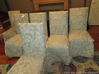 Six upholstered dining chairs arranged in a row showing light beige and cream leaf patterned removable covers.