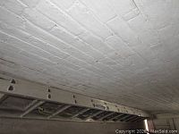 Partial view of one metal ladder stored horizontally against a wall, showing logo sticker and top part of ladder.