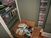 Box with assorted hardback books and part of the shelving rack with CDs and VHS tapes storing media items