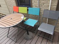 Foldable outdoor table with four foldable chairs showing colorful mesh backs and seats in orange, lime green, blue and gray.