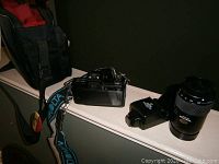 Minolta camera with attached lens, additional lens, flash unit, and strap on ledge showing condition and details
