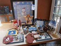Full assortment of snowman holiday decorations shown on a table including framed snowman print, various wooden figurines, snowman shaped signs, and small lamps.