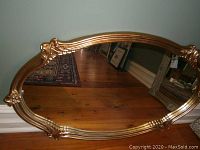 Oval wall mirror with gold-tone carved frame showing floral details and curved edges.