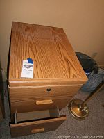 Photo of a two drawer wood file cabinet with natural wood grain finish and wooden handles shown in a room next to a brass-colored floor lamp.