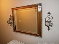 Full view of rectangular wall mirror with decorative gold and wooden frame with two black iron sconces on either side.