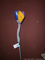 Floor lamp triple colorful flower-shaped shades with blue, yellow, and purple colors against red wall.
