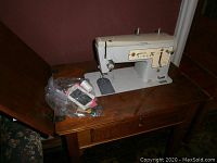 Singer sewing machine folded into wooden cabinet, angled view showing sewing machine and top closed wooden lid.