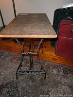 Full view of the table showing the wooden top surface and intricate Black iron base with detailed curved design and foot pedal area.