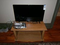 Black LG flat screen TV displayed on a wooden TV stand with remote and cables on top.