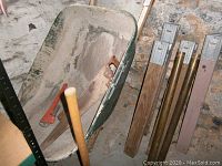 Full view of wheelbarrow, some wooden supports, and hand tools inside the wheelbarrow.