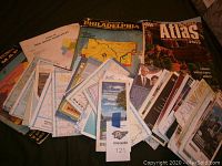 Full view of assorted maps spread out on table, including folders, atlases, and loose maps.