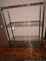 Full front view of the metal shelving unit on wheels with three wire shelves and chrome finish