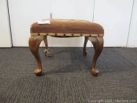 Side view showing wooden cabriole legs and nailhead trim along the bottom edge of the needlepoint cover