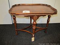 Wood veneered coffee table with scalloped pie crust edge and four turned legs connected by stretchers