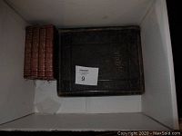 Four volume set of The Journals of Reverend John Wesley with visible wear on spines and an old black leather-bound family Bible with loose cover placed in a white box.