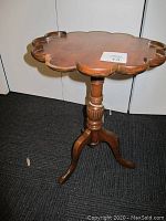 Front perspective view of vintage wooden pie crust table showing scalloped edges and pedestal base with tripod legs on dark carpet.