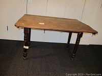 Front angle view of antique wooden kitchen table showing turned legs and worn top surface.