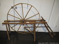 Wide view of the large wooden pendulum spinning wheel showing circular spoked wheel and wooden base with legs