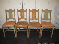 Front view of four vintage wooden kitchen chairs; two painted beige with peach seats on the outside and two bare wood chairs in the middle.