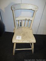 Front view of vintage white wooden chair showing worn paint, scratches, damaged decorative rods on backrest and repaired crack on top back rail.