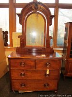 Front view of antique wooden dresser with attached decorative mirror showing three drawers with round wooden pulls and general surface wear.