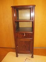 Full front view of wooden shelf telephone cabinet showing two open shelves, a central drawer with knob and pull, and a bottom cupboard door with knob. Cabinet wood finish is medium-dark with some wear marks.