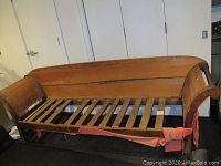 Wooden settee couch frame with slatted base, curved armrests and backrest, showing wear and scratches.