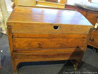 Front angled view of antique wooden storage bin showing hinged lid and keyhole area with some damage and scratches.