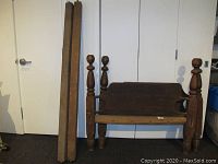 Bed frame parts arranged standing against a white wall showing the headboard or footboard with cannon ball finials and two long wooden side rails