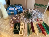 Photo shows multiple Christmas candles, LED light strings in original packaging, wired light strands, small red decorative candle, candleholders, potpourri bag, and a green Christmas towel with a tree design arranged on a countertop.