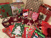 Wide view of assorted Christmas gift bags, tissue paper, ribbons, gift boxes, tags, and cards arranged on a surface showcasing a variety of holiday designs and colors.