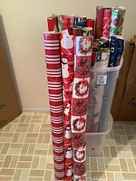 Several rolls of wrapping paper standing upright demonstrating different designs such as Christmas wreaths, snowmen, stripes, and bold colors.