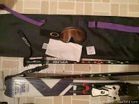 Salomon snow skis and Reflex poles with Oakley ski goggles on top of black gear bag.