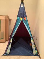 Front view of the kids teepee showing the open door with blue fabric and colorful flags near the top.