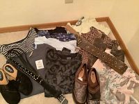 Photo showing various women's clothing mostly tops in patterns of stripes, floral, leopard accent and a graphic pink shirt, paired with three pairs of women's shoes including black flats, bronze flats, and brown ankle boots plus a brown studded belt and lace-trimmed piece.