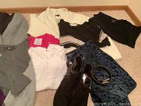 Overview of all clothing items laid on carpet including sweaters, tops, denim skirt, shoes, and belt.