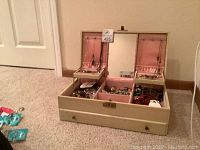 Front view of open jewelry box on beige carpet, showing top tray compartments, mirror, removal tray lifted.