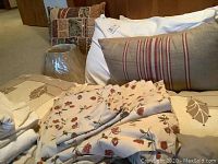 Photo of floral cotton sheets draped over bedding with decorative pillows and standard pillows in background.
