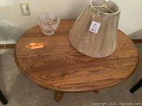 Photo of round wooden coffee table with small glass vase and fabric lampshade on top