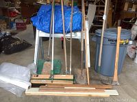 Full view of all items including saw horses, garden tools, broom, tarp, heavy plastic, and trash can arranged in garage or storage area.