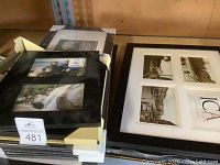 Black multi-photo frame with four slots and protective corners, stacked with other frames on a shelf.
