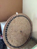Full view of 48 inch round stone table top showing mosaic pattern with tan, beige center and dark brown square tile border.