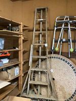 Full view of wooden ladder standing upright next to shelves and walkers, showing overall shape and height.