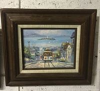Framed oil painting showing streetcar traveling down hill towards bay with sailboats and island in background, in dark wood frame with cream matting.