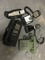 Lot of vintage telephones including green push-button, Motorola black phone, white cordless phone and two vintage intercom microphones.
