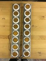 Pair of vintage strip lights viewed from above on a wooden surface, showing amber circular lenses in a silver metal housing with white guards.